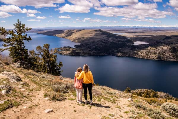Mom and daughter standing on a mountain overlooking a lake.