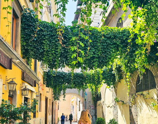 girl walking under vines hanging across street in Trastevere