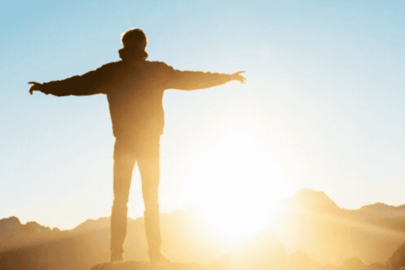 man on cliff looking at sunset