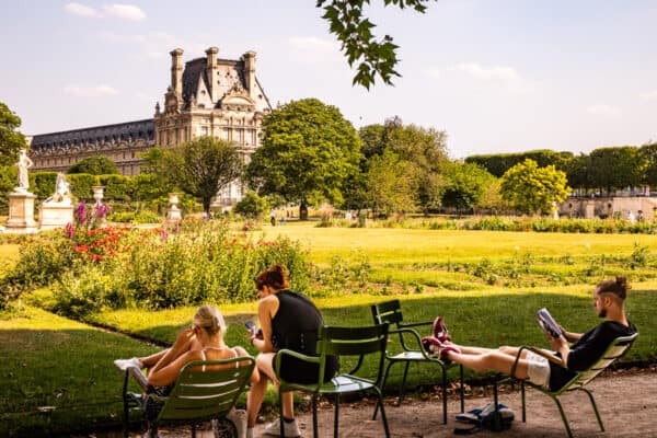 people sitting on chairs in Tuileries garden looking at louvre